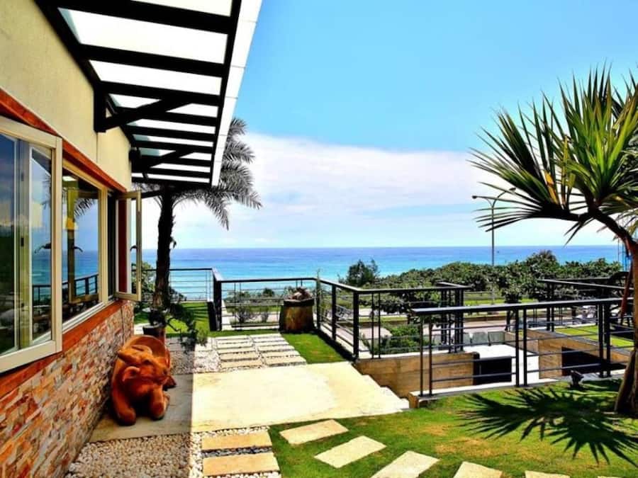 A coastal property with a patio, a view of the ocean, and a stone staircase leading to a deck.