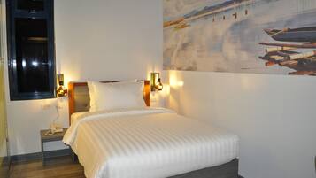 A hotel room with a bed, bedside lamps, a nightstand with a phone, and a painting of boats on the wall.