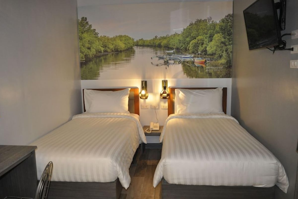 Habitación de hotel con dos camas, una mesita de noche, un teléfono y un televisor montado en la pared.
