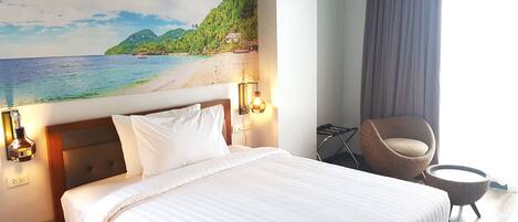 A hotel room with a bed, a chair, a wall-mounted lamp, and a painting of a beach scene.