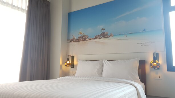 A hotel room with a bed, two wall-mounted lamps, and a painting of Boracay White Sand Beach. - GQ Plaza (Kalibo)