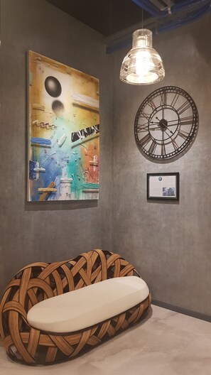 A room with a woven bench, a large abstract painting, a clock, and a hanging light fixture. - GQ Plaza (Kalibo)