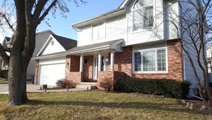 A two-story house with a brick facade, white siding, and a garage.