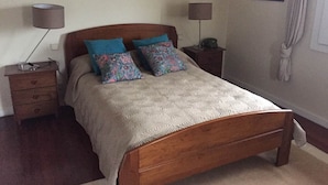 Een slaapkamer met een houten bed, twee nachtkastjes, een lamp en een kunstwerk aan de muur.