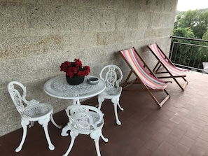 A patio with a round table, two ornate chairs, a striped hammock, and a potted plant with red flowers.