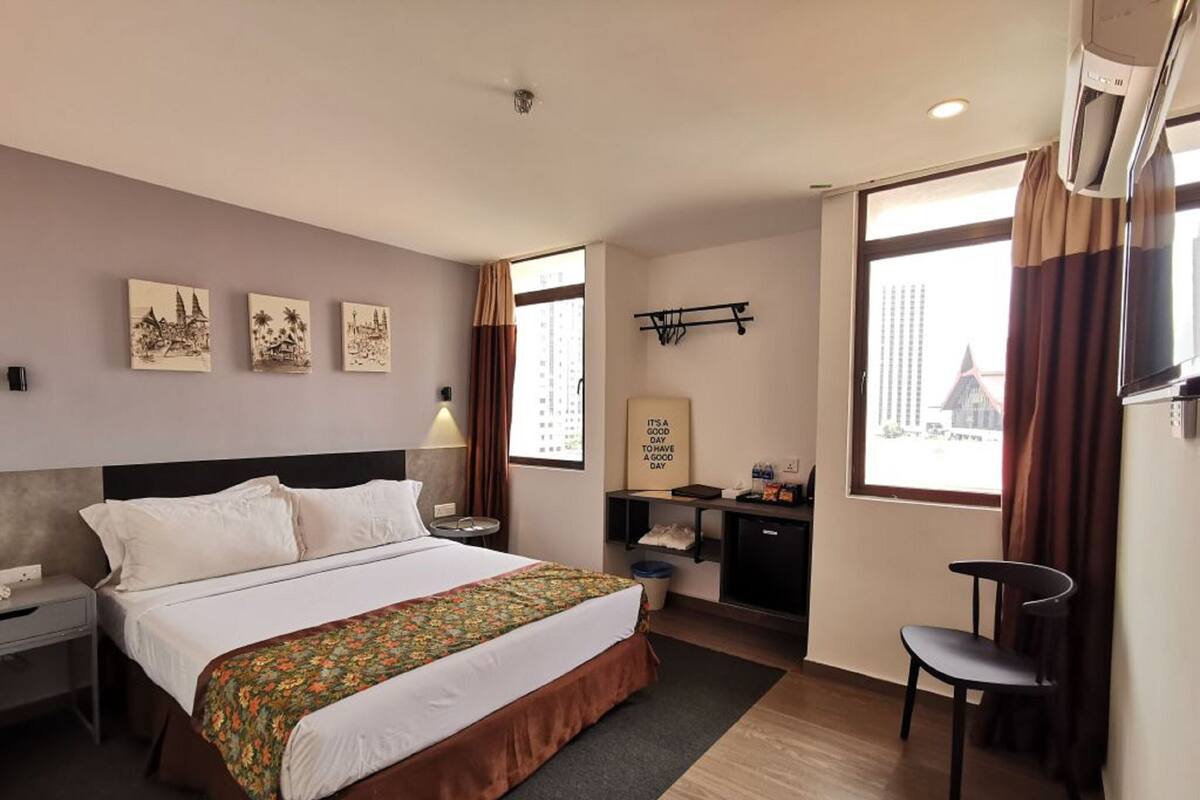 A hotel room with a bed, a desk, a chair, and a window with curtains.