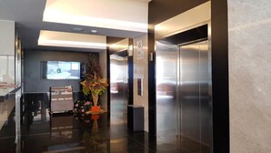 Un ascensor moderno con pantalla digital, una mesa de recepción y un arreglo floral.