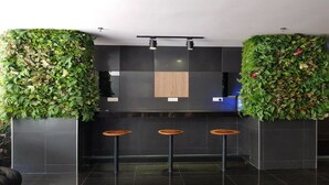 Zona de bar moderna con paredes de baldosas oscuras, taburetes de madera y jardines verticales verdes a cada lado.