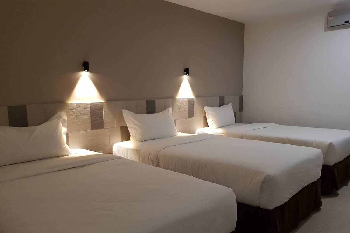 A hotel room with three single beds, each with a headboard and bedside lamps.