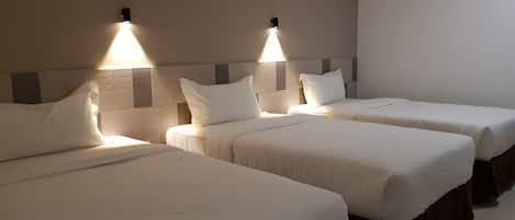 A hotel room with three single beds, each with a headboard and bedside lamps.