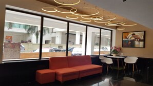 Un vestíbulo moderno con un sofá rojo, una mesa redonda con sillas y ventanas grandes que dan vista a coches estacionados y edificios.