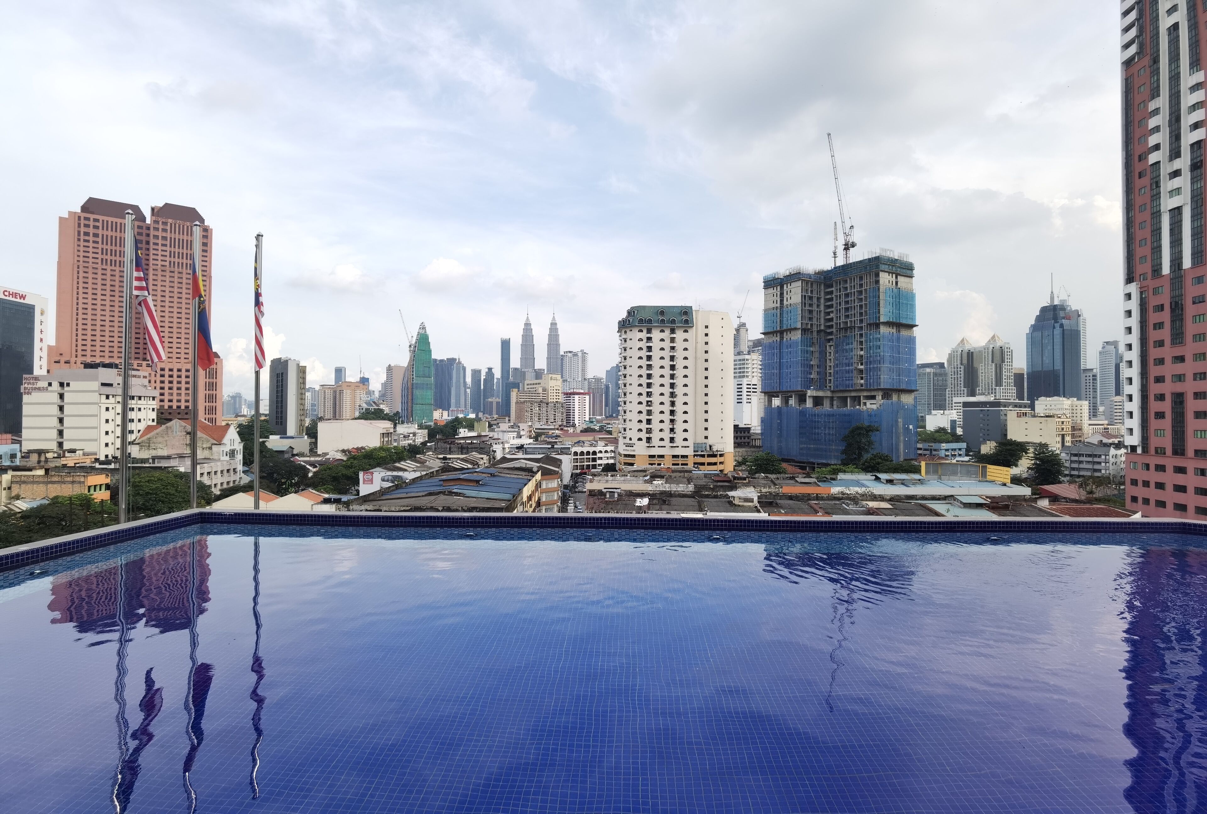 A rooftop pool with a city skyline in the background, including several high-rise buildings and a construction crane.