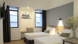 Habitación de hotel con dos camas, una mesita, una lámpara, un adorno en la pared y vistas a la ciudad.