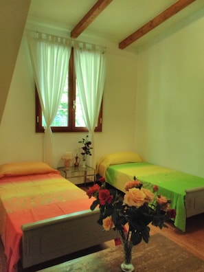 Een slaapkamer met twee bedden, een nachtkastje, een vaas met bloemen en een raam met gordijnen.