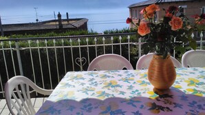 A table with a floral tablecloth, a vase with flowers, and a view of mountains and a body of water.