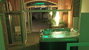 A hot tub in a room with a brick wall and a glass door leading to another area. - Alla Corte dei Bertoli SPA - Casa Gioele (Canale)