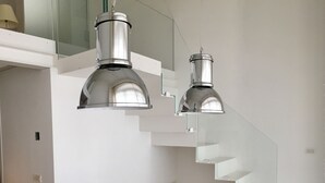 A modern dining area with a wooden table, four chairs, and two pendant lights. A staircase with glass railings is visible in the background. - Alla Corte dei Bertoli SPA - Casa Gioele (Canale)