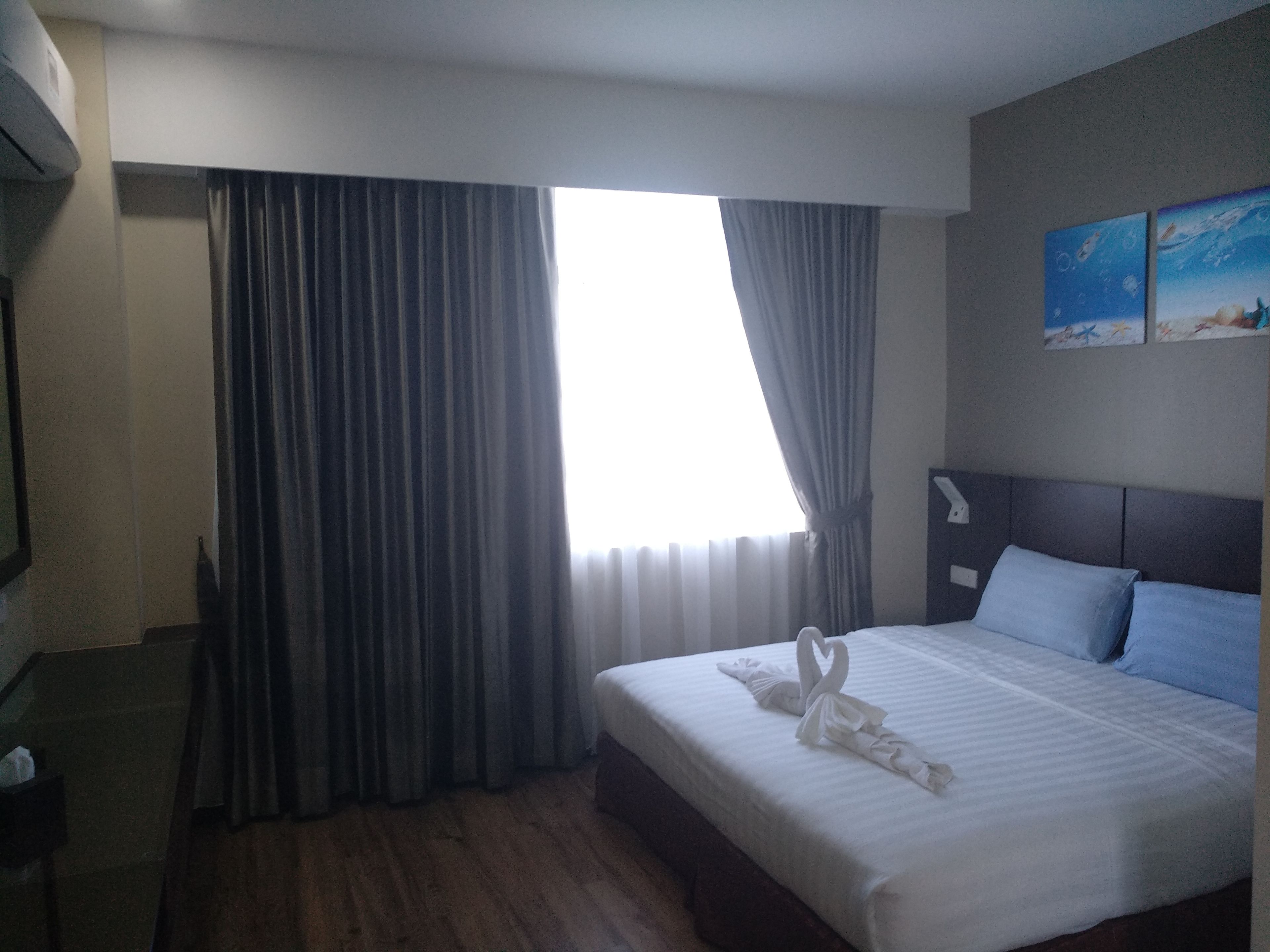 A hotel room with a large bed, a headboard, a nightstand, a lamp, and a painting on the wall.