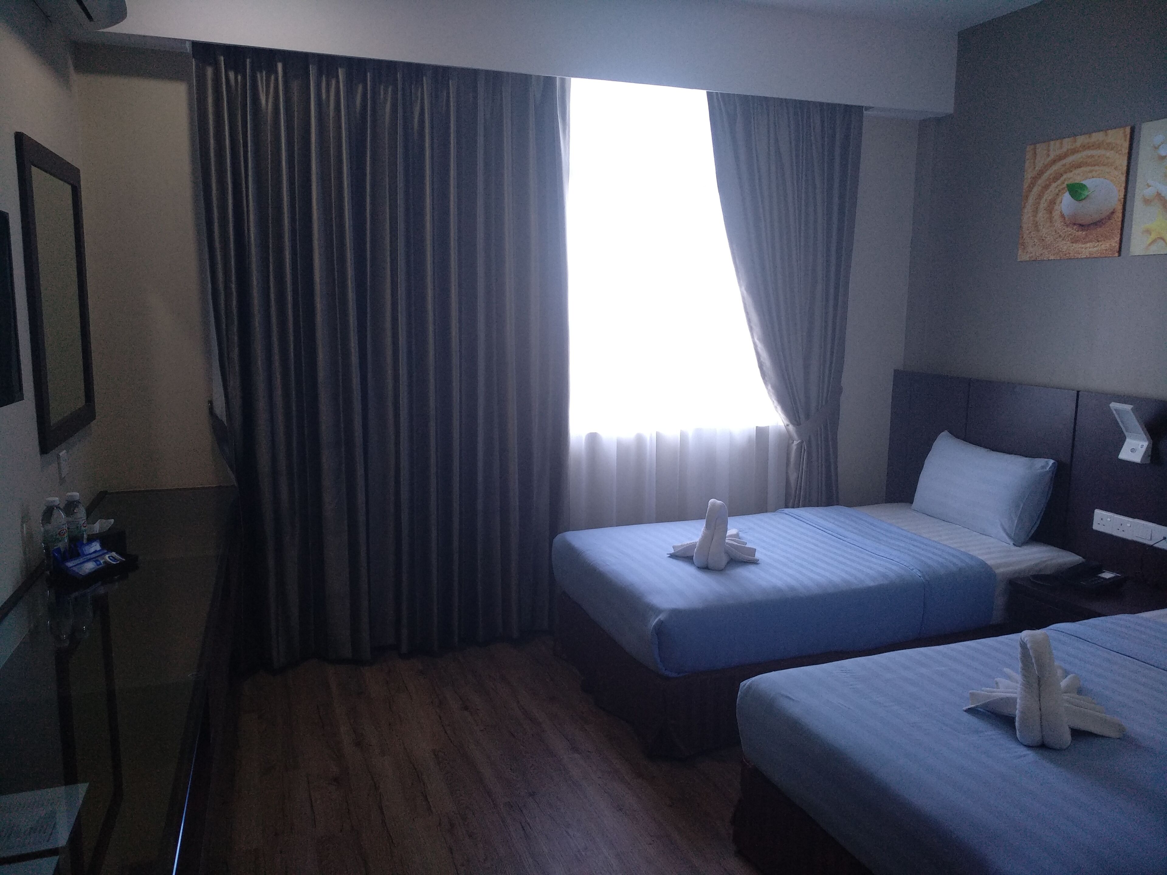 A hotel room with two beds, a nightstand, a mirror, and a window with curtains.