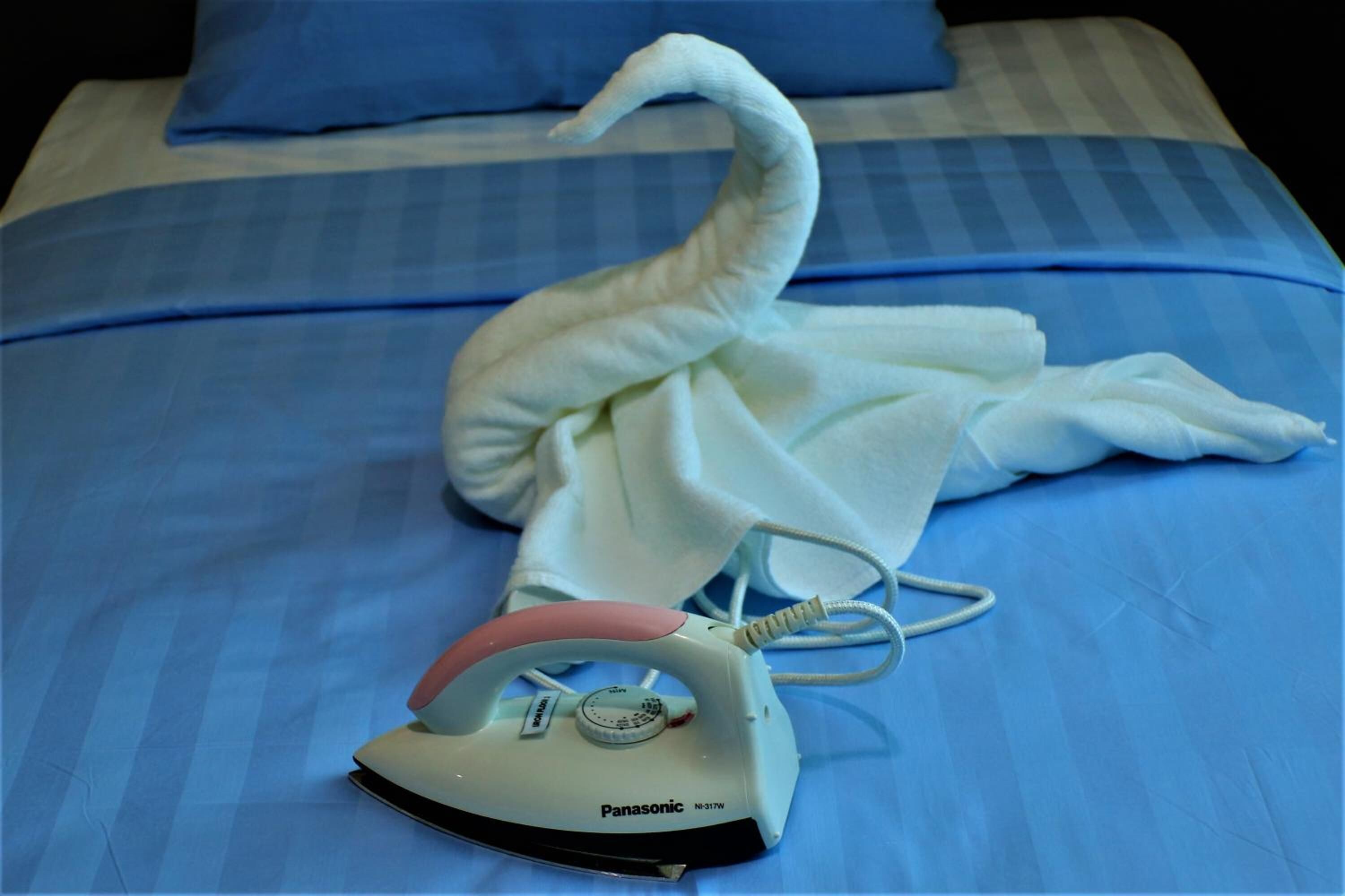 A bed with a blue bedspread, a white pillow, and a swan-shaped towel.