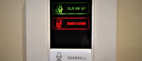 A wall-mounted intercom system with a green "CLEAN UP" sign, a red "DO NOT DISTURB" sign, and a doorbell button.