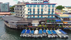 Un hotel frente al agua con un edificio grande, un muelle con barcos y una zona de bar.