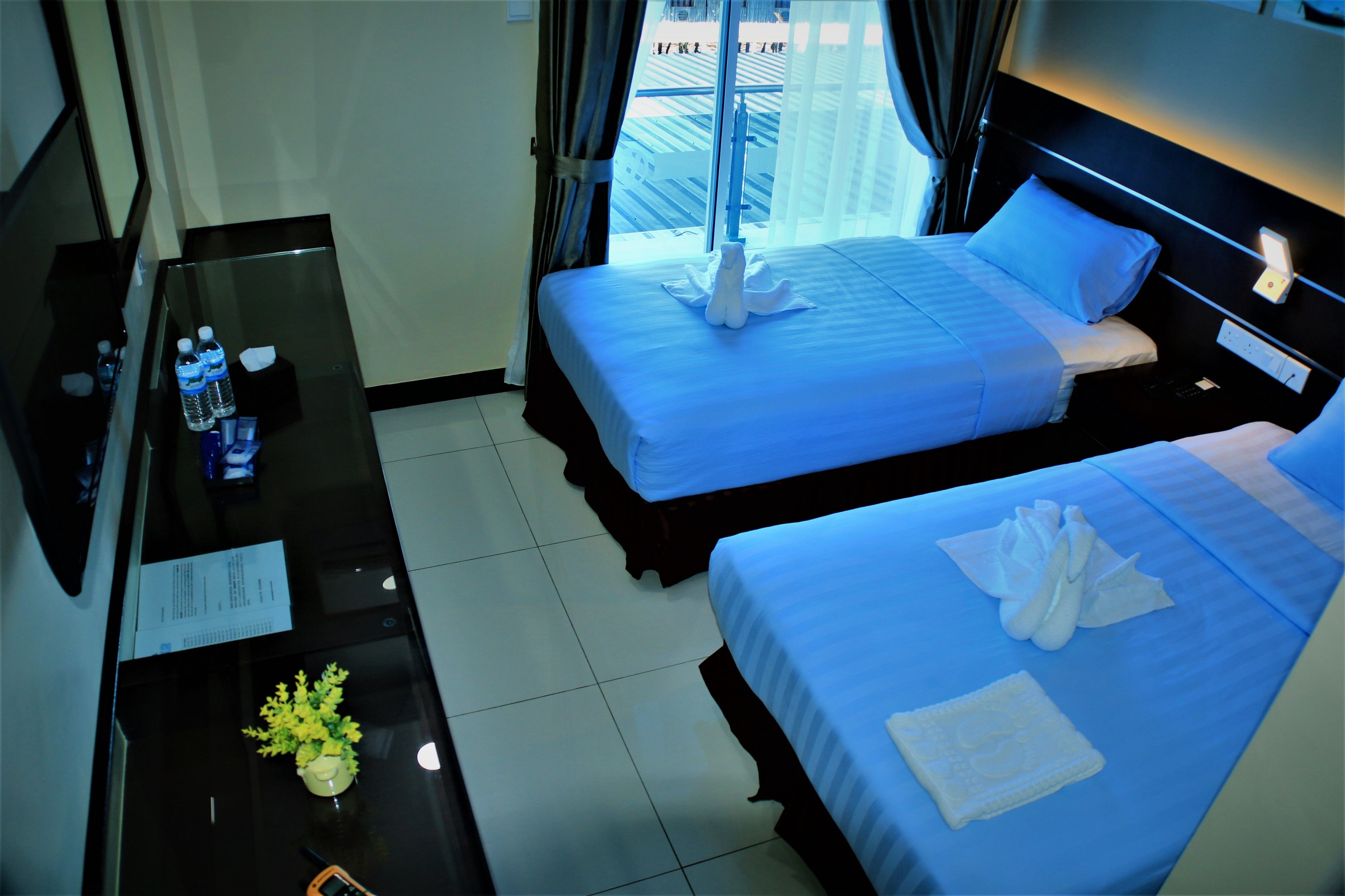 A hotel room with two beds, a desk with a chair, a TV, and a window with curtains.