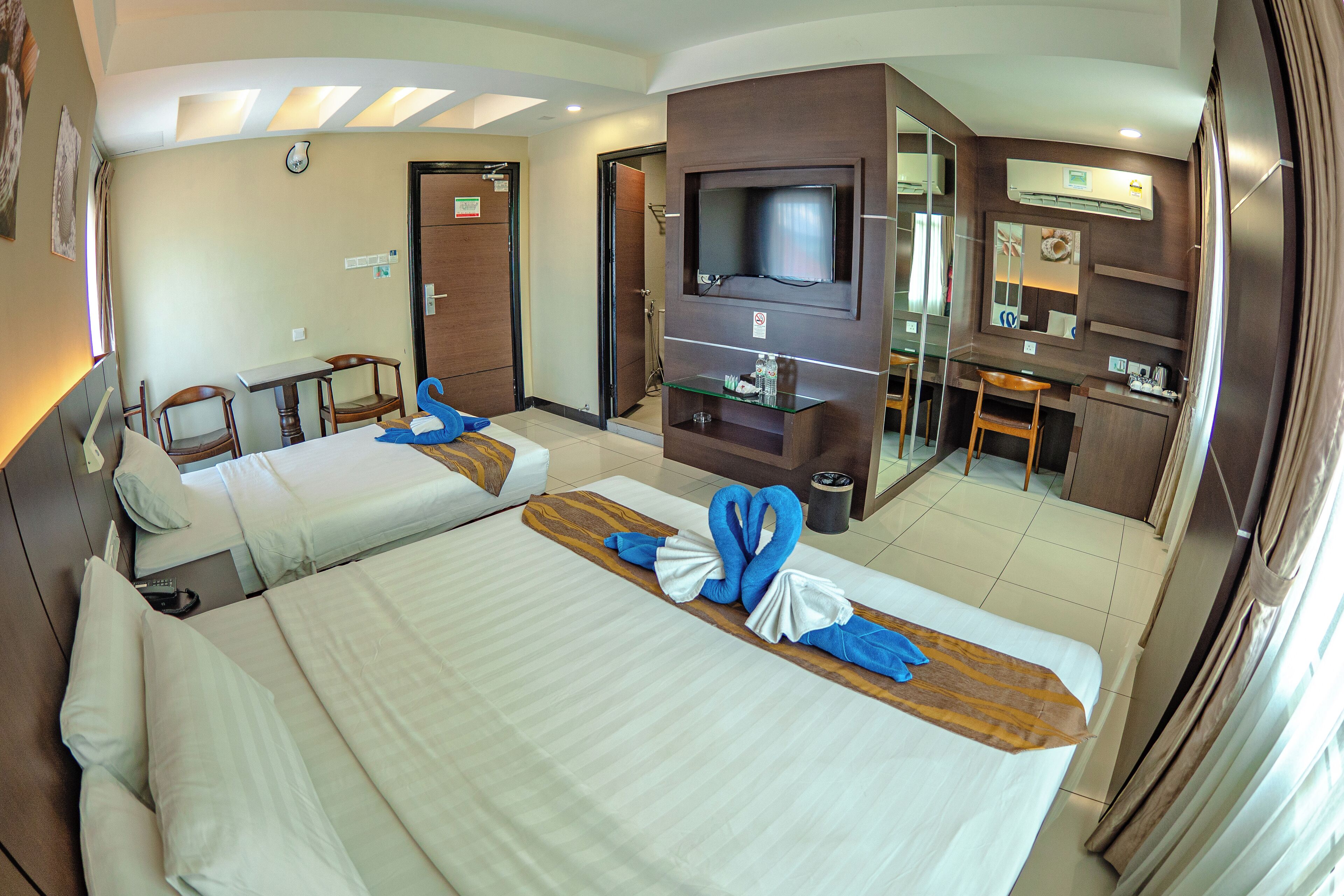 Ein Hotelzimmer mit zwei Betten, einem Fernseher, einem Schreibtisch und einem Badezimmer.