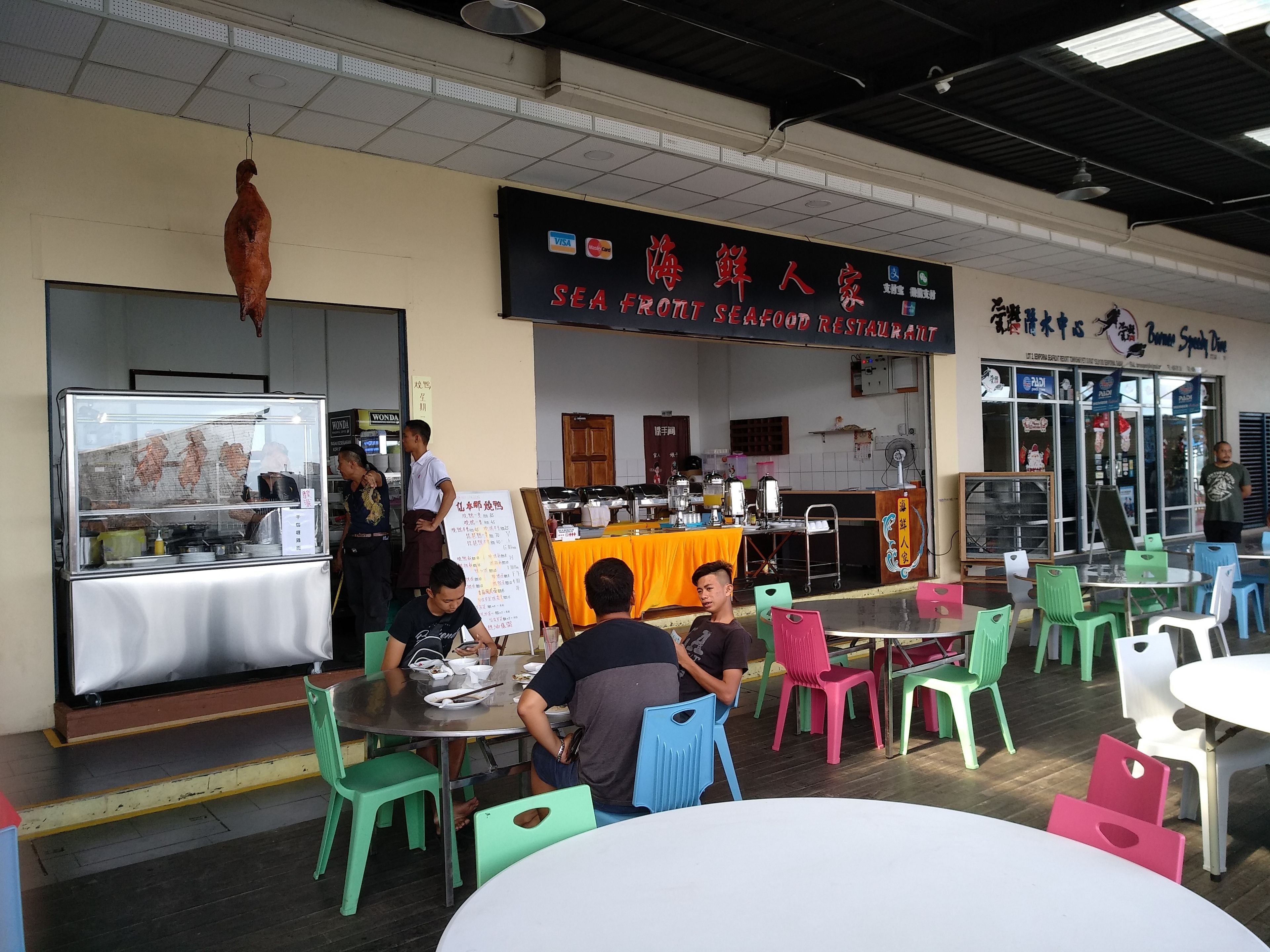 Ein Fischrestaurant mit einer Beschilderung in einer Fremdsprache, Außenbereich mit bunten Plastikstühlen und einer Theke mit Lebensmitteln.