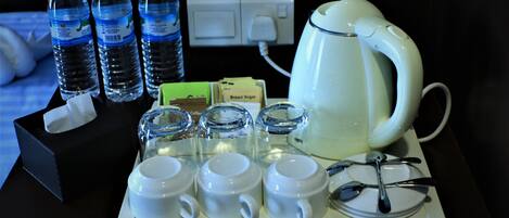 A hotel room's breakfast setup with a coffee maker, tea kettle, cups, and bottles of water.