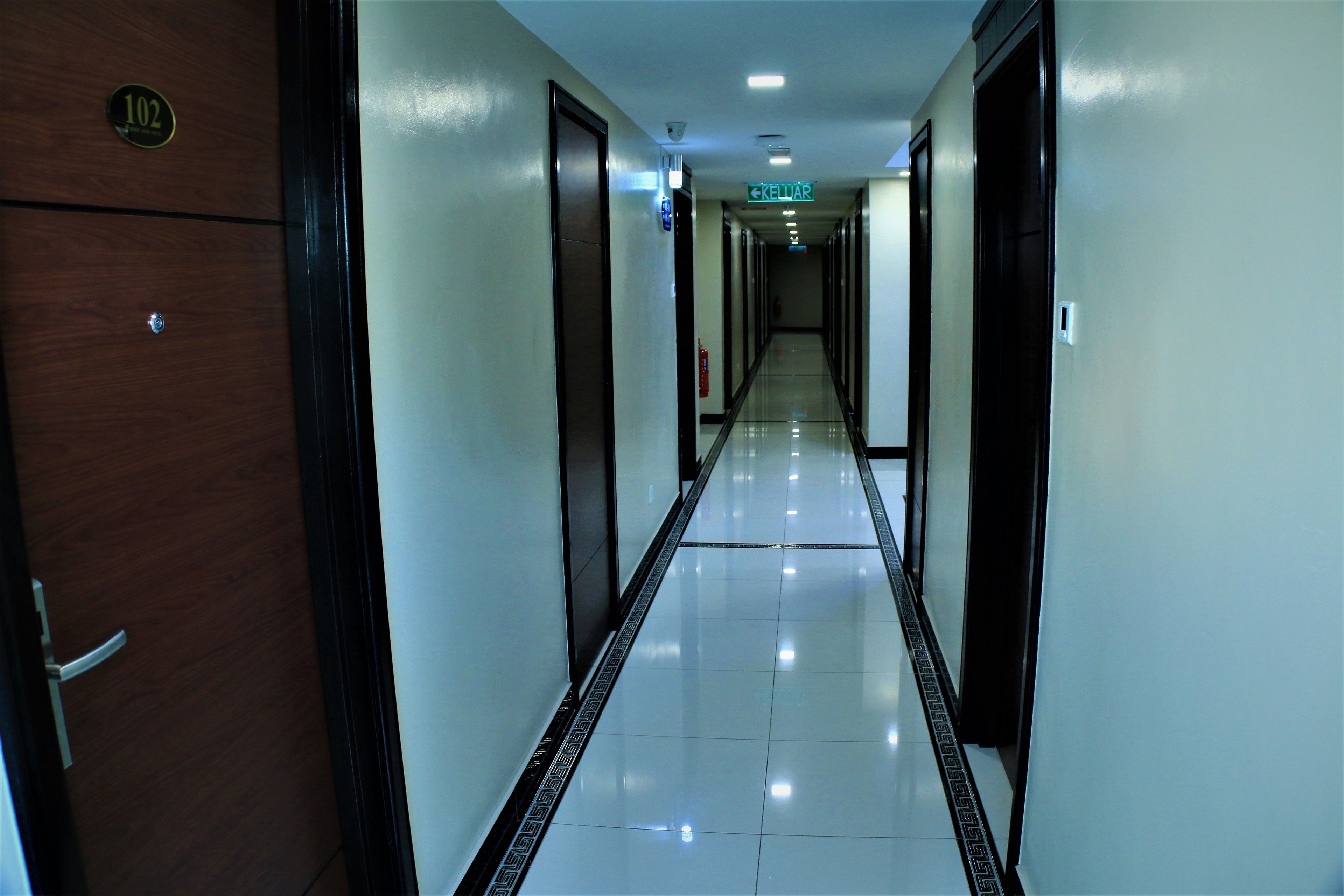 A hotel hallway with a reflective floor, doors on both sides, and a sign indicating the direction to the lobby.