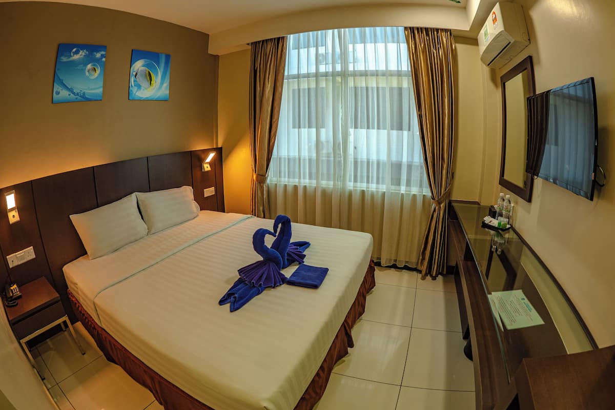 A hotel room with a bed, a nightstand, a desk, a mirror, and two paintings on the wall.