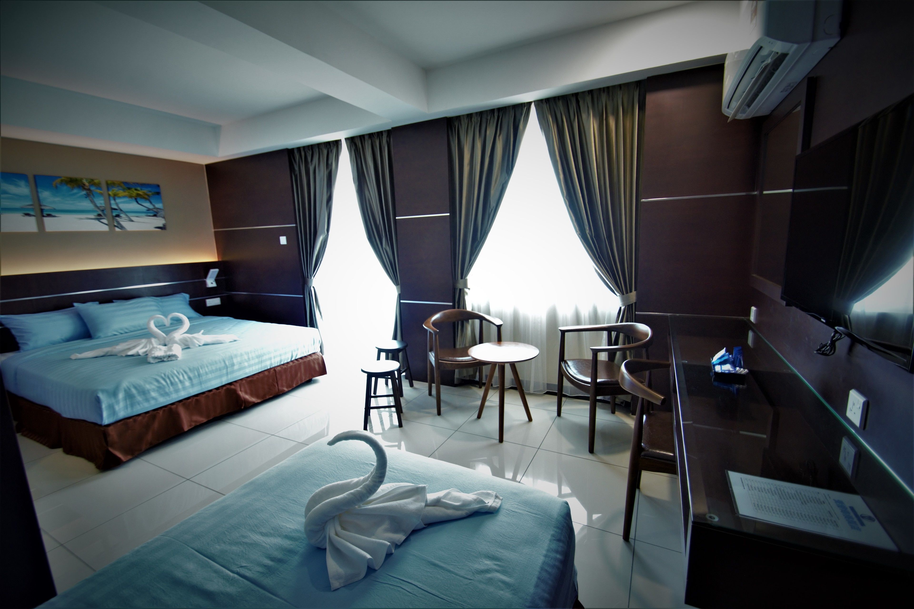 A hotel room with two beds, a desk, a chair, and a small table.