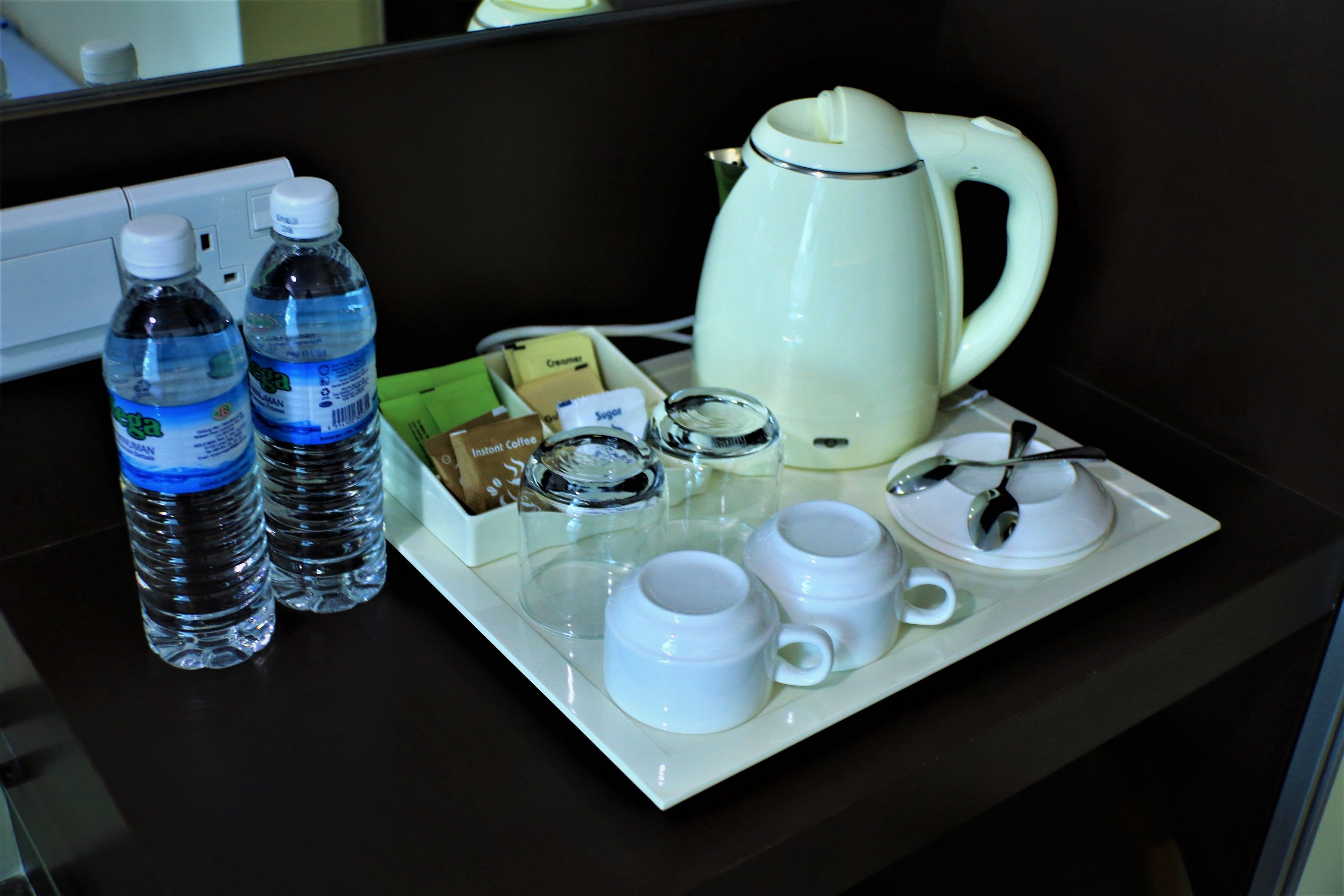 A tray with two water bottles, a coffee pot, sugar packets, a creamer, a sugar bowl, and two white cups with a spoon.