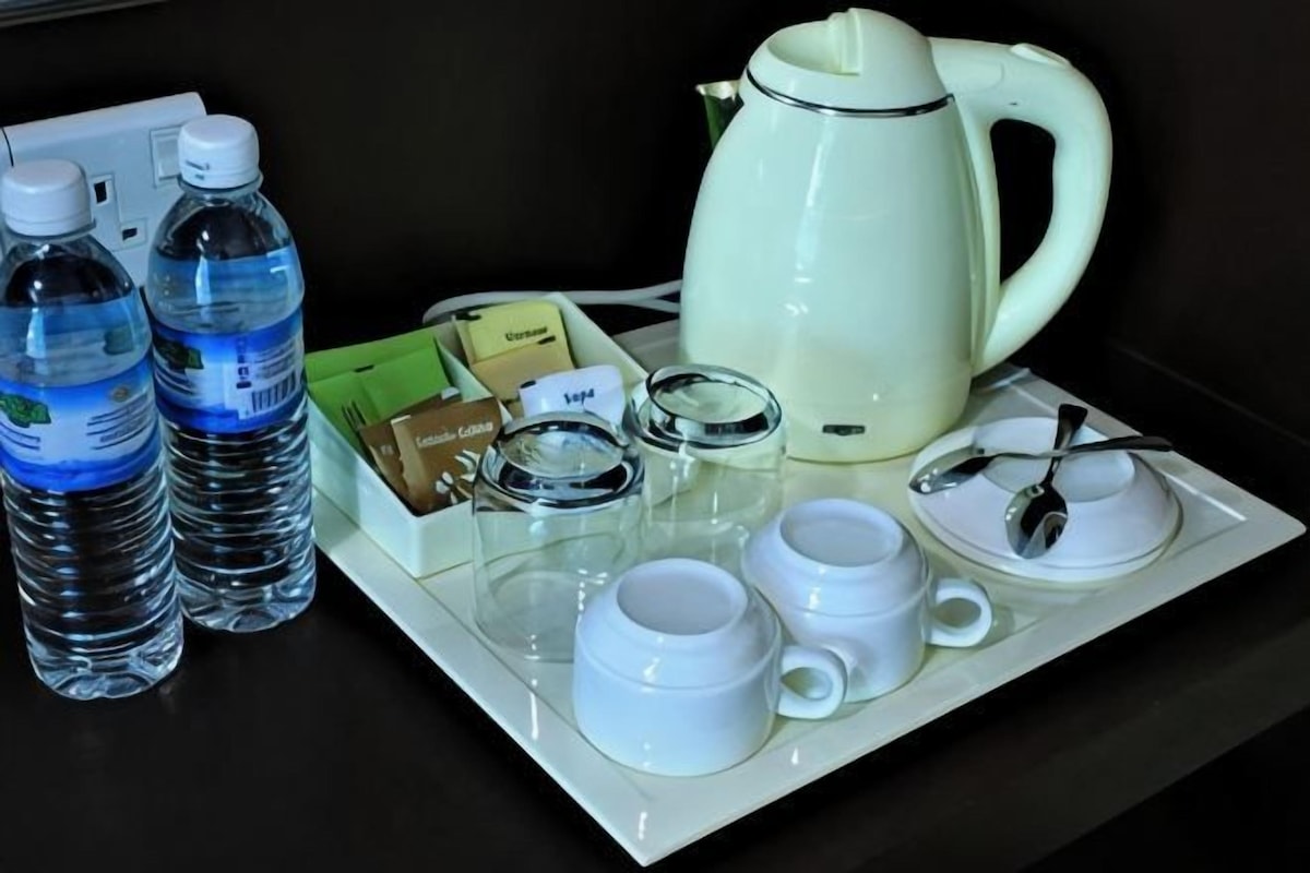 A tray with a white kettle, two water bottles, a glass container, and a set of white cups and saucers.
