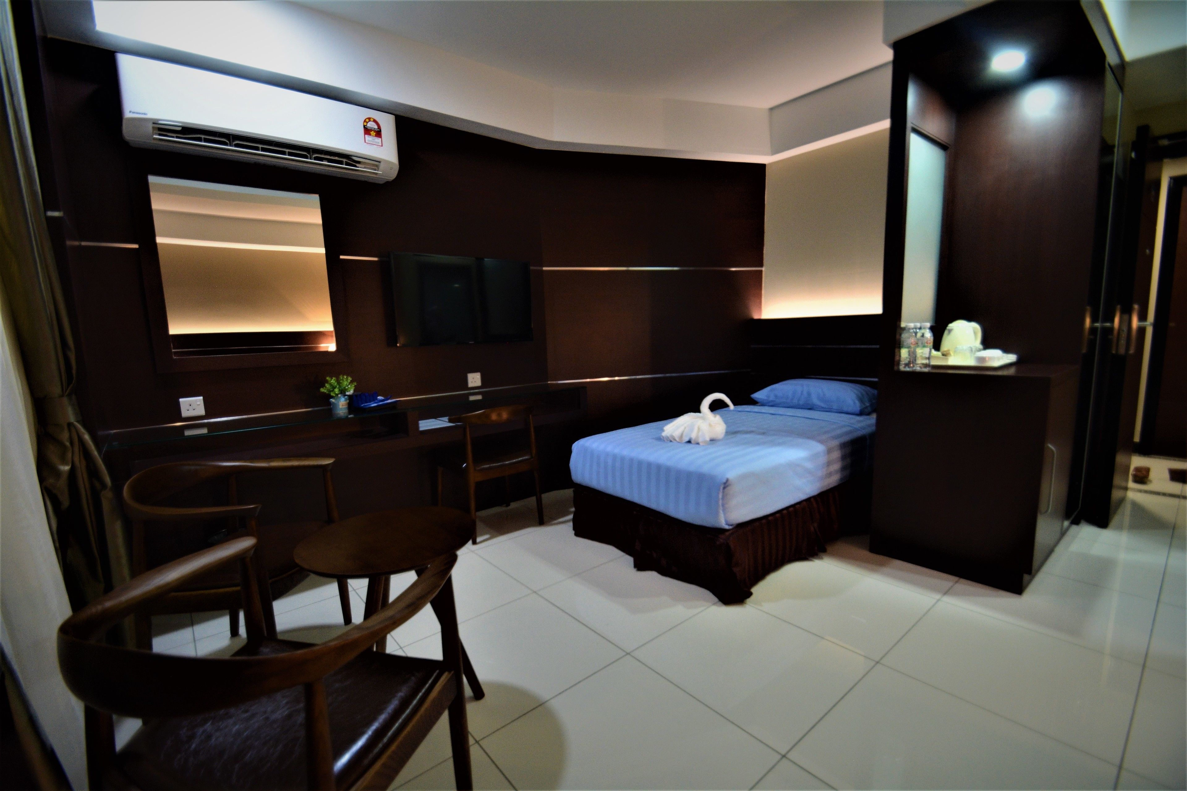 A hotel room with a bed, a desk, a chair, a mirror, and an air conditioning unit.