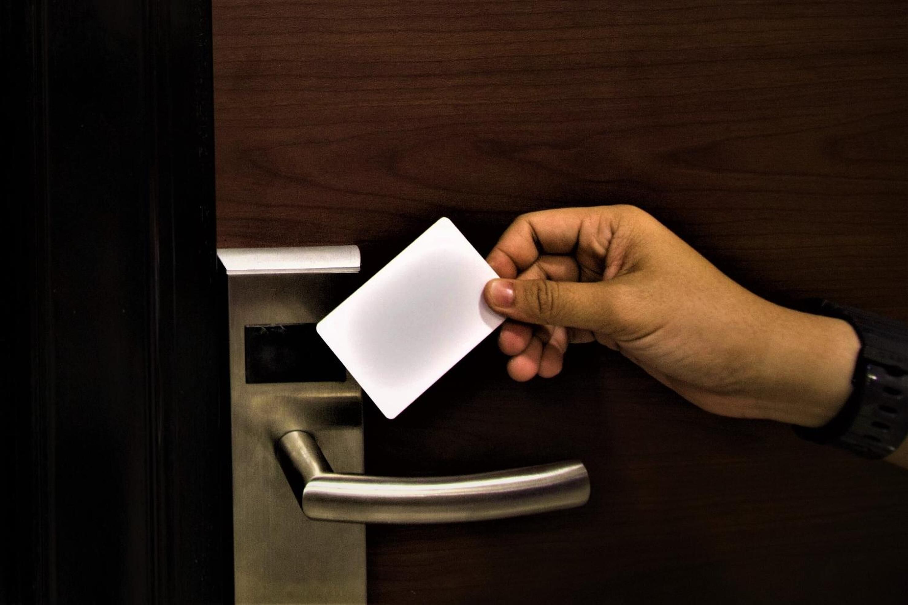 A hand holding a white card near a door handle.