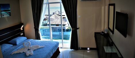 A hotel room with a bed, a TV, a desk, and a view of a building and water through the window.