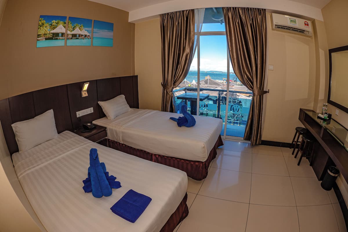 A hotel room with two beds, a desk, a chair, and a large window with a view of a distant cityscape.