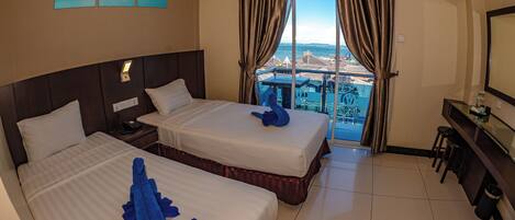 A hotel room with two beds, a desk, a chair, and a large window with a view of a distant cityscape.
