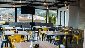 Un restaurante con sillas amarillas y negras, sofás grises y una amplia pantalla de televisión.