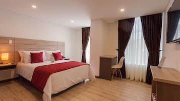 Una camera d'albergo con un letto, un comodino, una lampada, una scrivania, una sedia e tende.