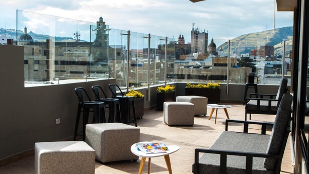 Una terraza en la azotea con mobiliario, una mesa y vistas panorámicas de la ciudad.