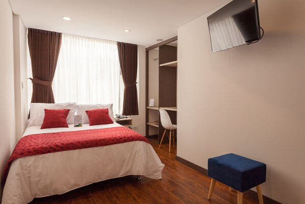 A hotel room with a bed, a desk, a chair, and a TV mounted on the wall.
