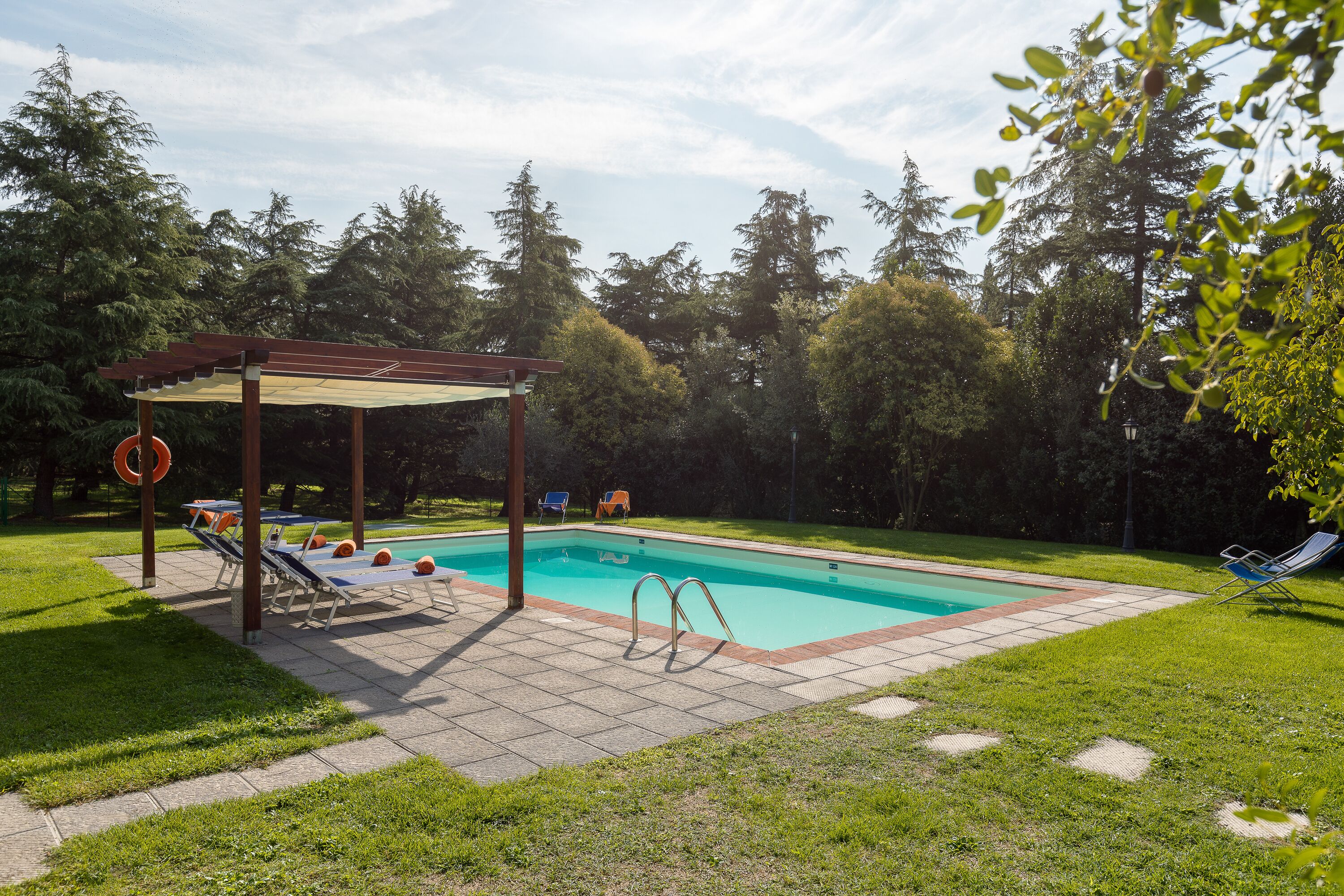 A rectangular swimming pool with a pergola and lounge chairs in a backyard.