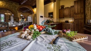 A rustic kitchen with stone walls, wooden beams, and a dining area with a table set for a meal. - Large stone manor with 8BR and 7BA, extended grounds, large fully-equipped pool. (CORTONA)