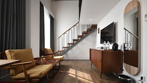 A modern living room with a staircase, wooden furniture, a flat-screen TV, and a large mirror. - Hotel Monopoli (Jakarta)