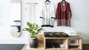 A neatly organized hotel room with a wooden bench, a plant, and a shelf with shoes and a towel. - Hotel Monopoli (Jakarta)