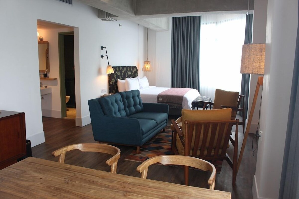 A hotel room with a bed, a sofa, a dining table, and chairs.