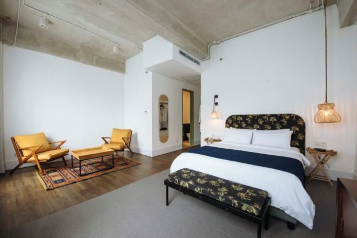 A bedroom with a bed, two chairs, a bench, and a hanging light fixture.